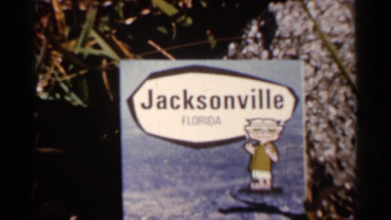 A 1966 Florida home-movie frame shows a Jacksonville Florida sign with a cartoon figure, photographed close up beside foliage and a tree trunk.