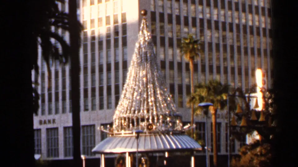 A 1966 Jacksonville home-movie frame shows a large illuminated Christmas tree in a downtown plaza, backed by palm trees, street lamps, and mid-century building facades.