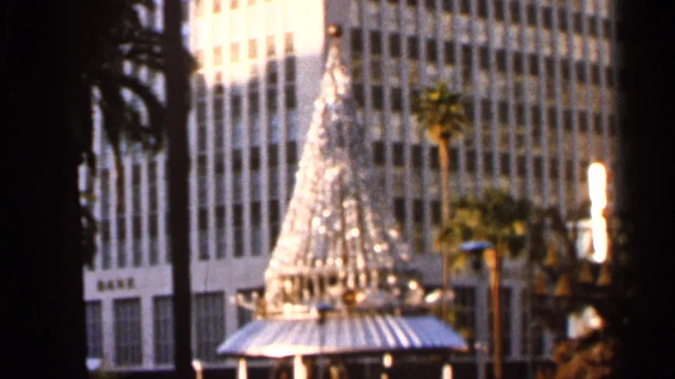 A soft 1966 Jacksonville frame holds on a lit Christmas tree in a downtown setting, with palm trunks, street lighting, and tall building windows in the background.
