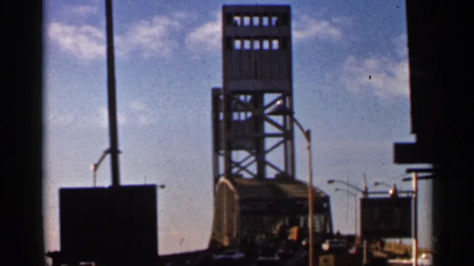 1966 Florida home-movie view of the John Alsop Jr. Bridge tower framed by dark foreground edges, with signs and streetlights nearby.