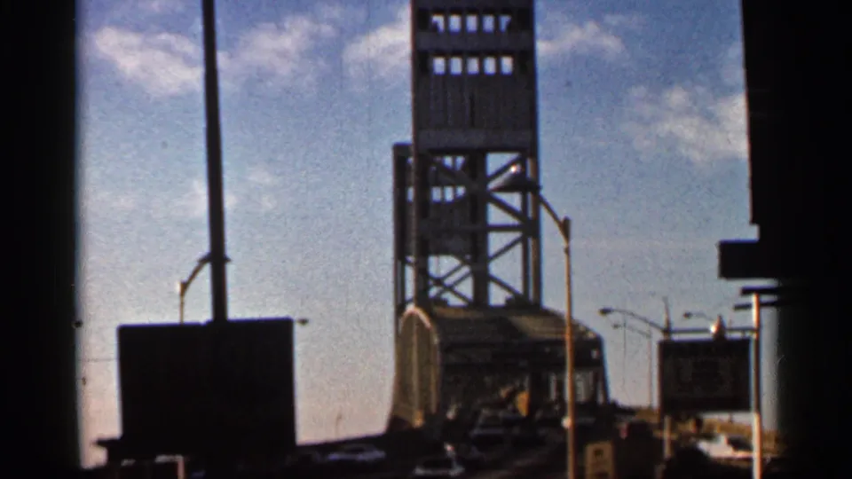 1966 Florida frame showing the John Alsop Jr. Bridge tower, overhead sky, road signs, and dark foreground framing from a passing viewpoint.