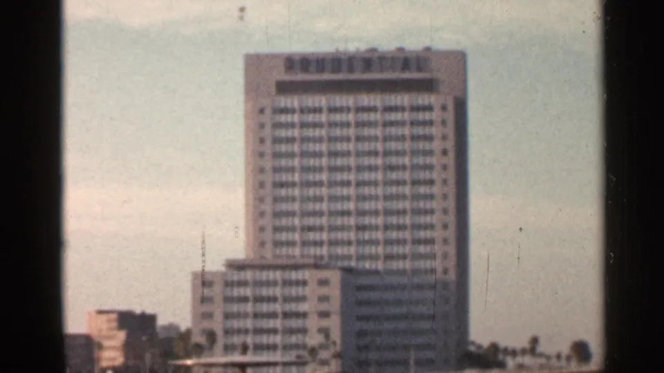 1966 Florida home-movie frame showing a tall modern high-rise and lower buildings in soft focus.