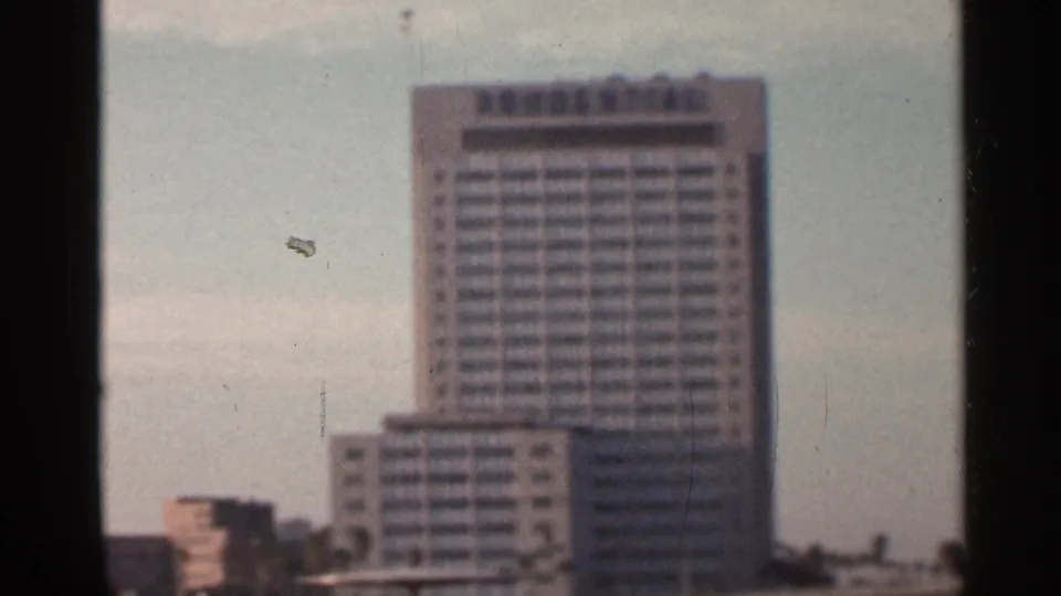 1966 Florida home-movie still of a tall gridded building with smaller waterfront structures below.