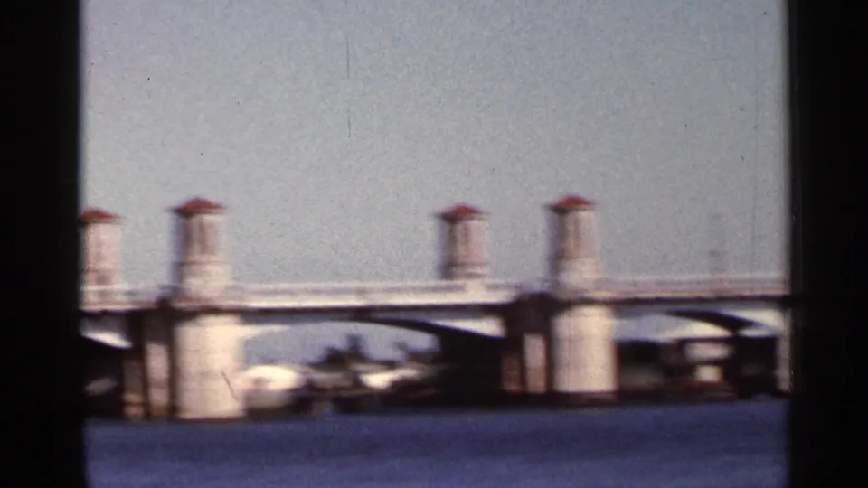 1966 Florida home-movie view of a broad bridge over water, with pale bridge supports and blurred cars crossing.