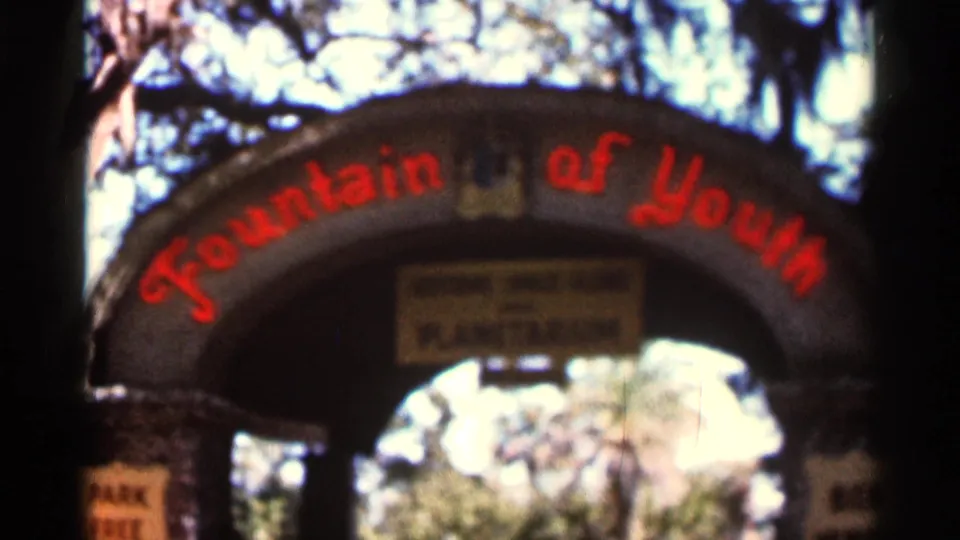 1966 Florida 8mm frame of the Fountain of Youth archway, with red lettering across the stone curve and a bright tree-filled entrance beyond.