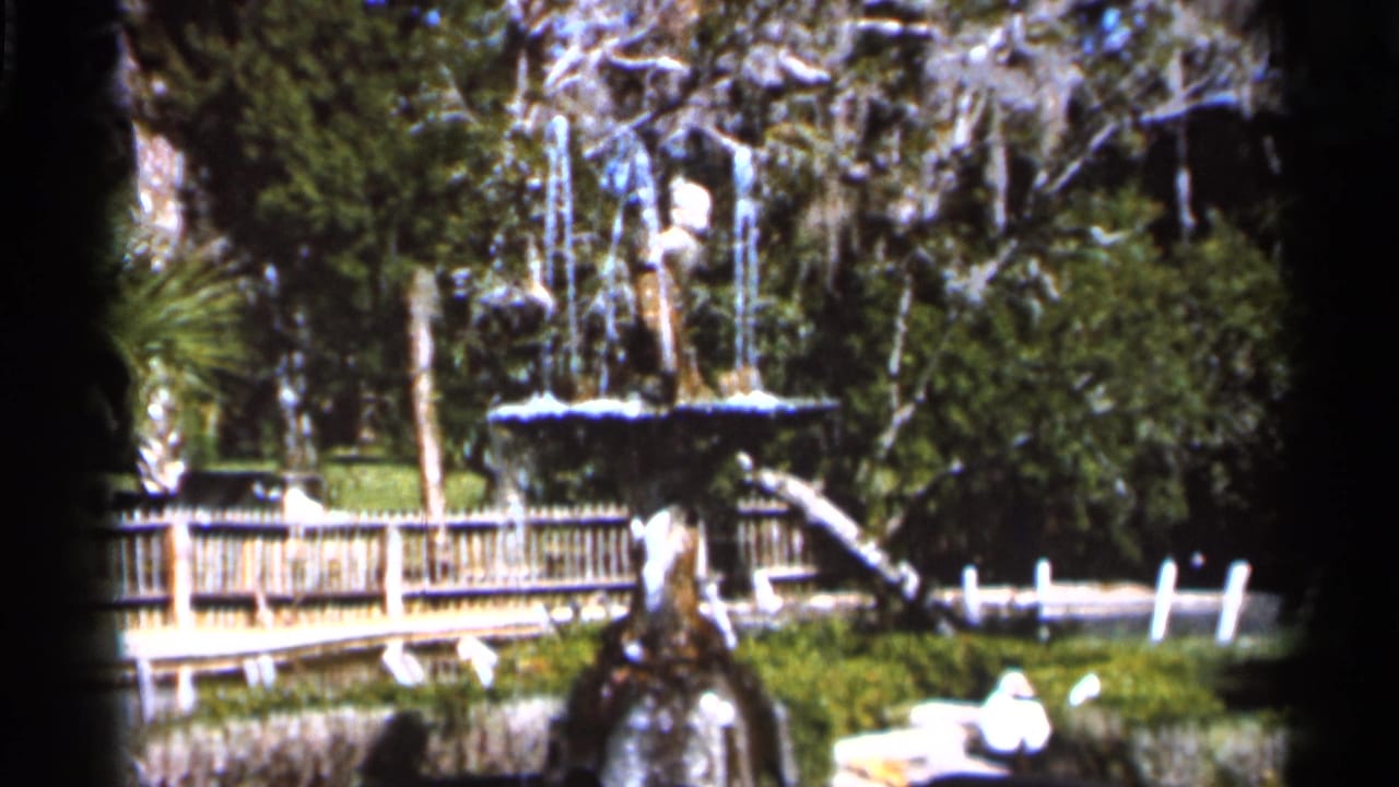 Fountain and wooden park structure surrounded by trees and greenery.