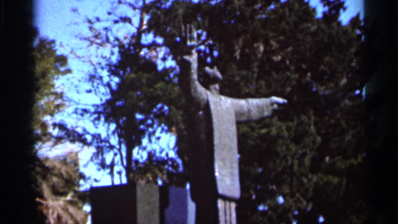 1966 Florida 8mm frame showing a robed outdoor statue with outstretched arms against trees and blue sky.