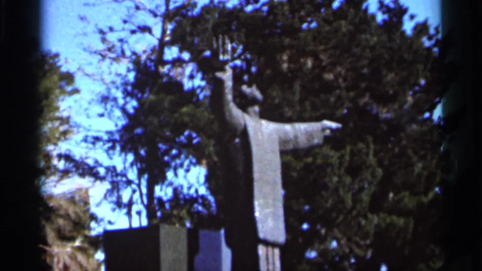 1966 Florida home-movie frame of a robed statue in a wooded area, with bright sky and film-edge shadowing.