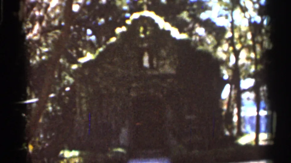 1966 Florida 8mm frame showing a rough stone or masonry building in a wooded area with ivy and bright backlight.