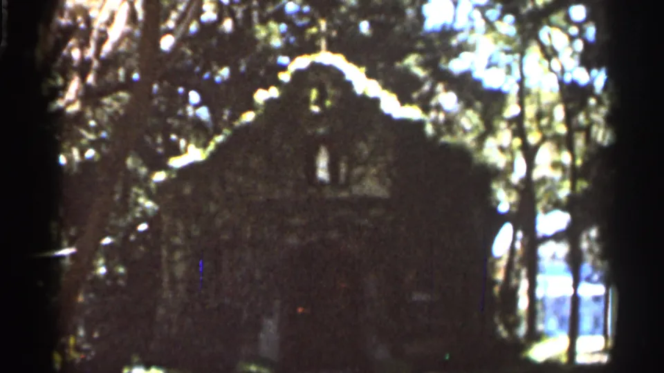 1966 Florida home-movie frame with a rustic structure silhouetted in trees, surrounded by dappled woodland light.