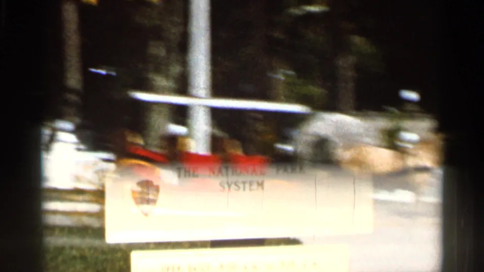 Soft 8mm frame with motion blur as the carriage passes behind a partially visible National Park Service sign.