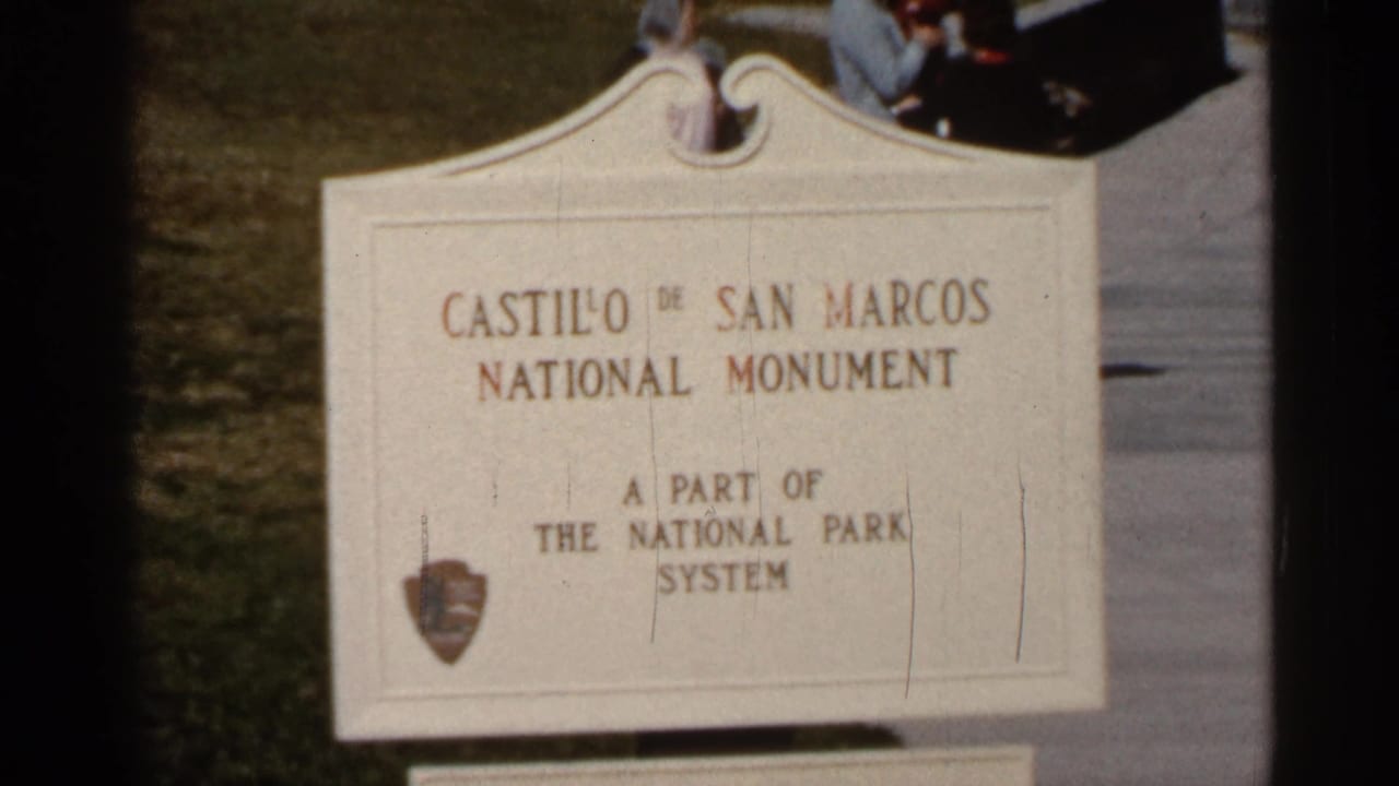 White Castillo de San Marcos National Monument sign beside grass and pavement.