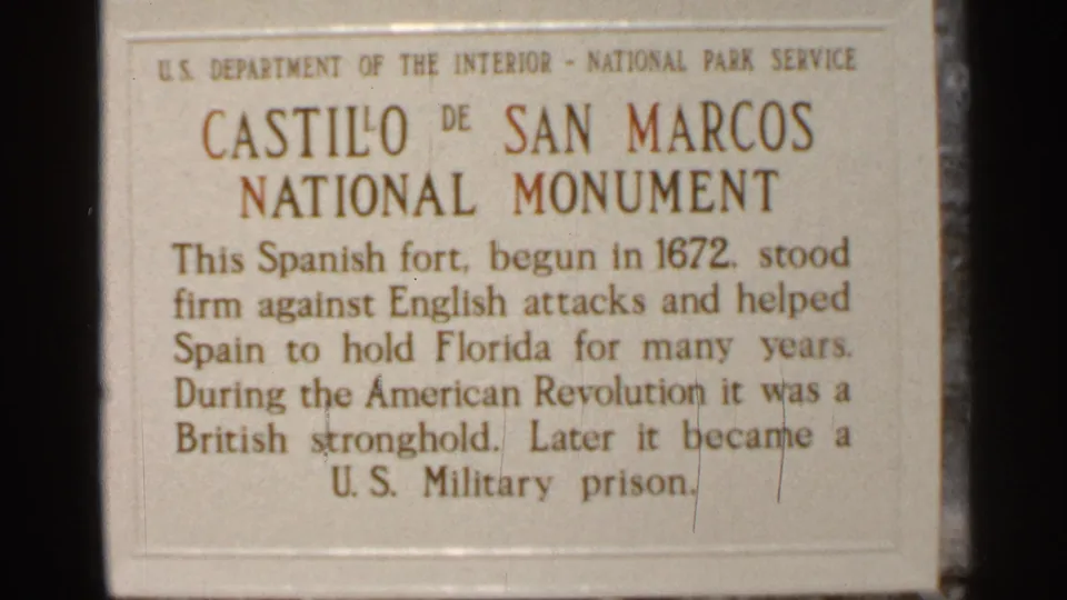 1966 Florida home-movie frame centered on the NPS plaque text for Castillo de San Marcos National Monument.