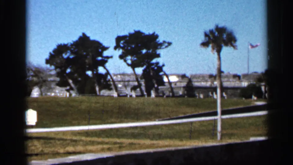 Color 8mm frame of Castillo de San Marcos grounds in Florida, showing trees, lawn, path, fort wall, and flag.