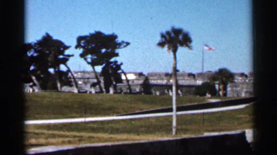 Visitor-shot 1966 view of Castillo de San Marcos with the fort partly framed by trees and an American flag.