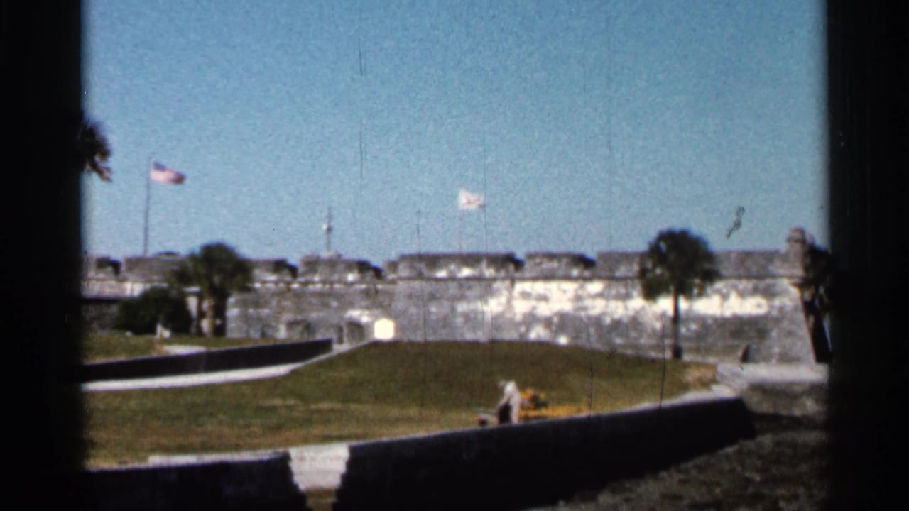 1966 Florida 8mm frame showing a stone fortress, likely Castillo de San Marcos, seen from a visitor viewpoint with flags overhead.