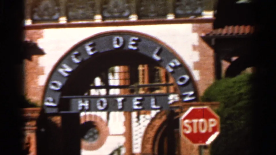 1966 Florida 8mm frame showing the Ponce de Leon Hotel entrance arch, red stop sign, shrubbery, and sunlit facade details.