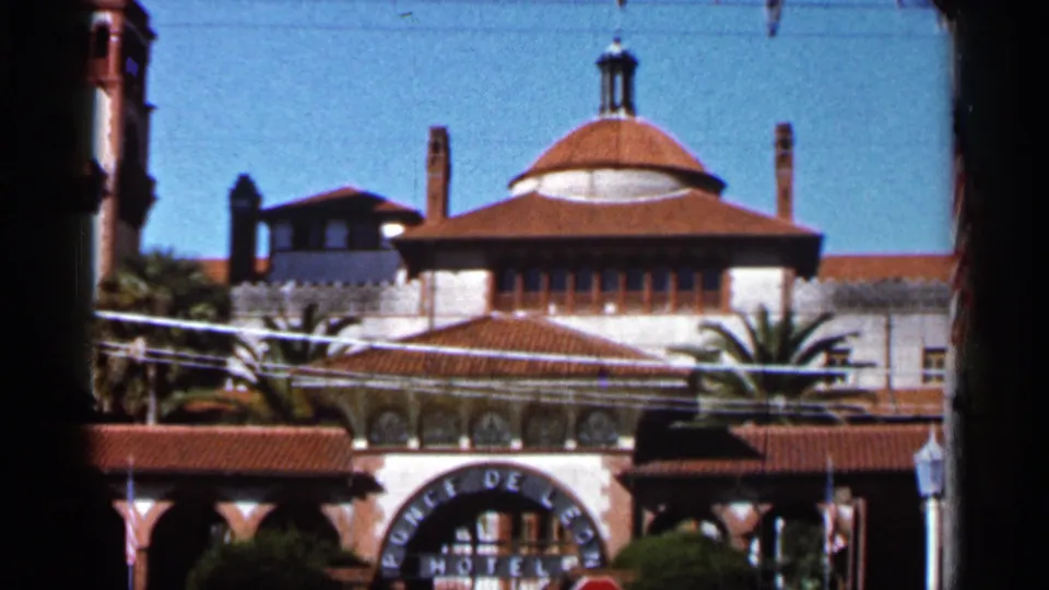 1966 Florida home-movie frame of the Ponce de Leon Hotel entrance with Spanish-style rooflines, palms, and partial entrance lettering.
