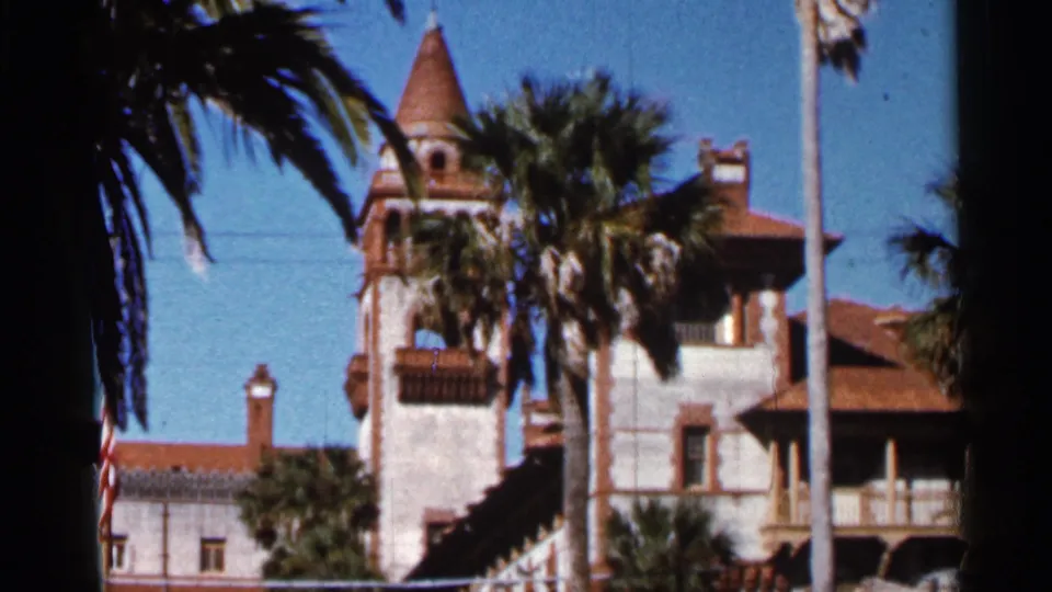 1966 Florida home-movie view of the Ponce de Leon Hotel tower and rooflines framed by palms, with a flagpole in the foreground.