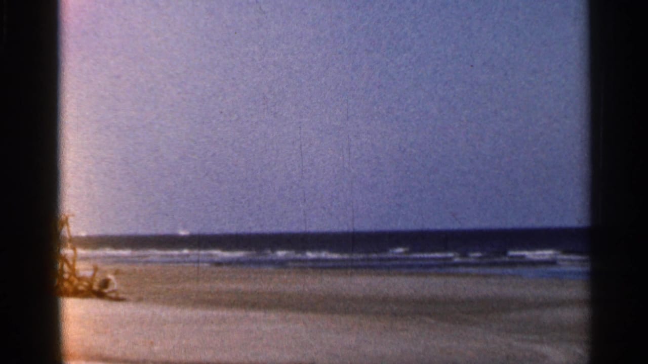 1966 Florida 8mm frame showing a quiet beach, low surf, pale sky, and heavy film gate edges.