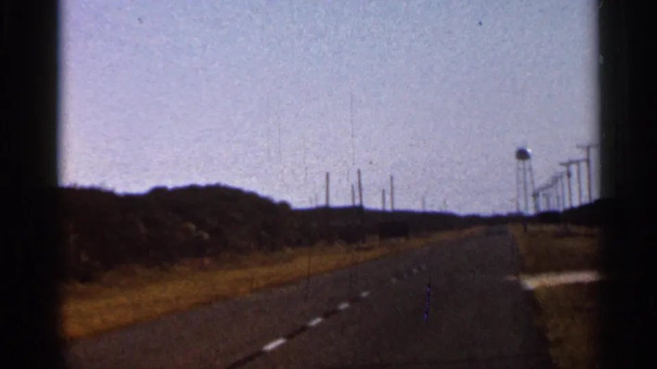 1966 Florida 8mm road frame showing a rural roadway, utility poles, low vegetation, and a distant water tower.