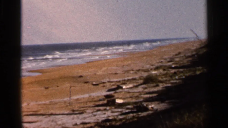 1966 Florida beach view showing rolling waves, sandy shore, scattered driftwood or debris, and soft 8mm color.