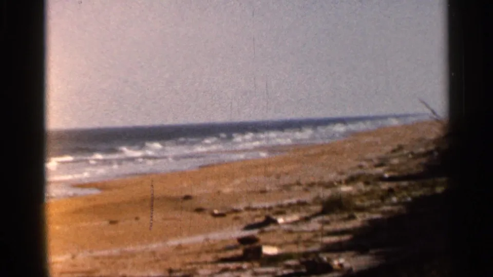 1966 8mm coastal shot of Florida surf and a sandy beach with scattered shoreline debris and visible film wear.