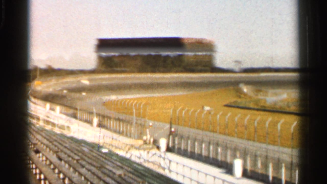 Empty racetrack grandstands beside a paved oval track and grass infield.