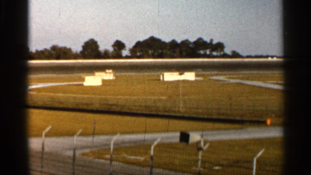 Wide racetrack view with grassy infield, fencing, and distant trees.
