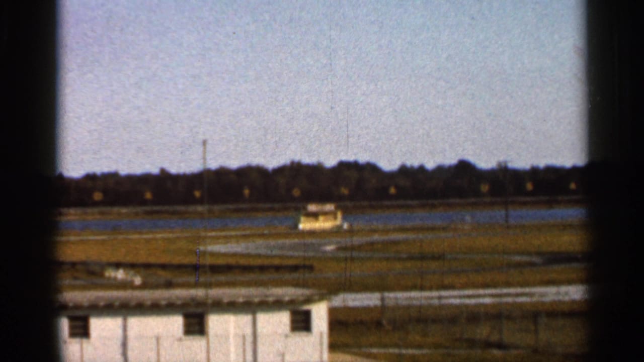 Distant race car on a racetrack behind a safety fence and small white building.