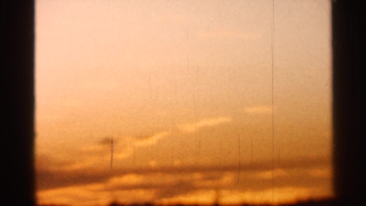 1966 Florida 8mm frame showing an orange sunset through dark window framing, with low clouds and film scratches visible.