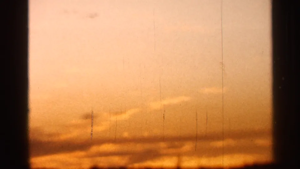 1966 Florida home-movie frame of a golden-orange sky divided by dark window trim, with thin clouds and visible 8mm wear.