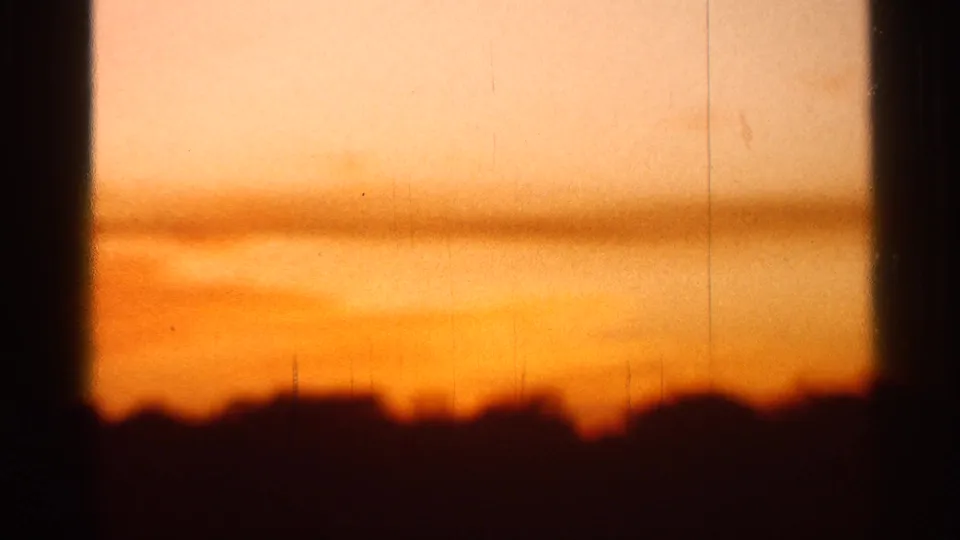 1966 Florida 8mm frame showing a low dark horizon under an orange sunset, bordered by heavy window trim and film wear.