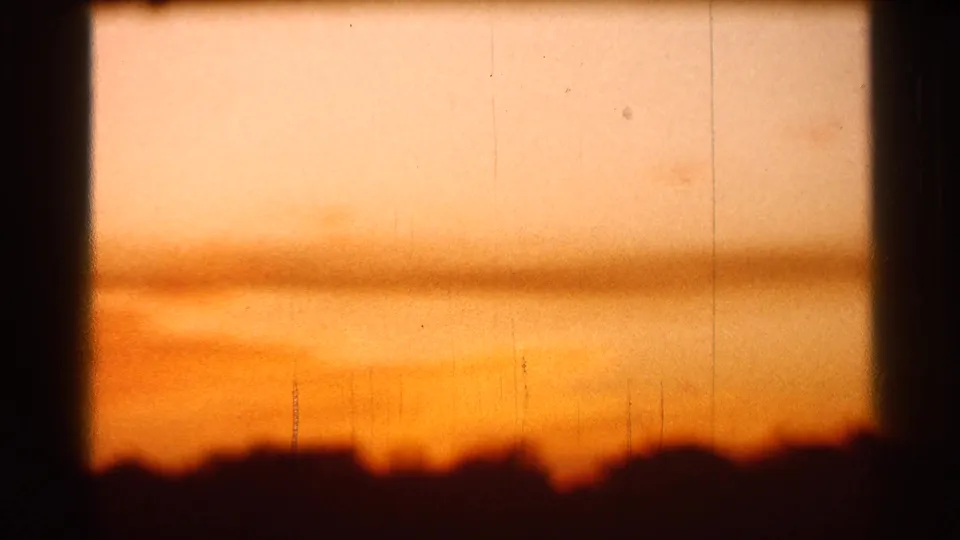 1966 Florida home-movie frame of an orange sunset through window trim, with a faint distant tower or antenna near the horizon.