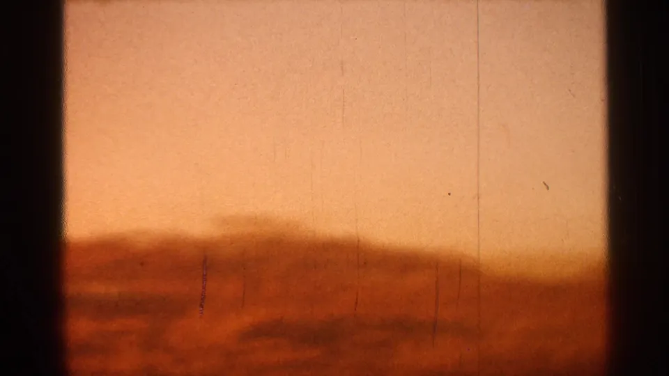 1966 Florida 8mm frame with a low rounded horizon, pale amber sky, soft cloud or haze bands, grain, scratches, and dark edge shadows.