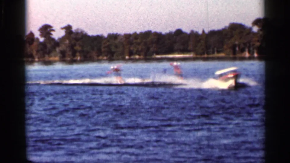 Three skiers appear in a line behind the boat wake on a 1966 Florida lake, with trees along the far shore.