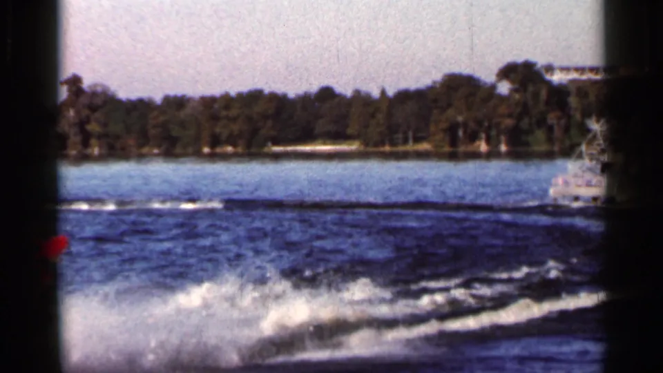 1966 Florida 8mm frame focused on churned boat wake and spray, with open water and a tree-lined shore beyond.