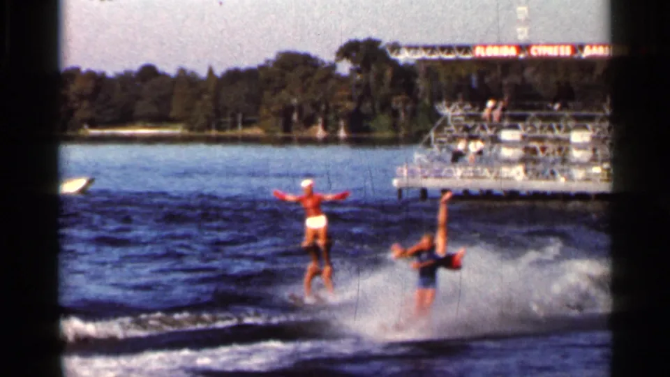 At the end of the 1966 Florida water-ski pass, one performer stays upright as the other tips into the lake spray.