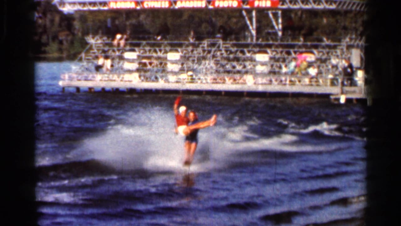 Water skier in a red top skims across a lake near spectator stands.