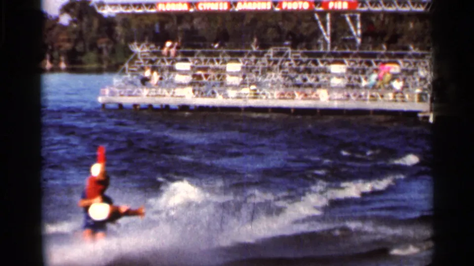1966 Florida 8mm frame showing the skier in a stunt position over lake spray, with spectator seating behind.