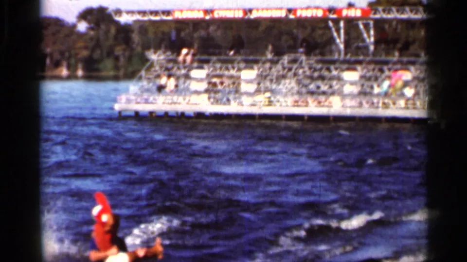 1966 Florida 8mm frame with the water skier low in frame and a large lakeside spectator stand across the background.