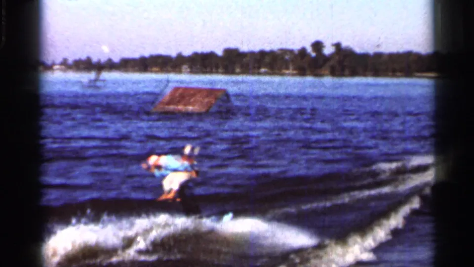 1966 Florida 8mm frame showing a water skier near a floating ramp, with open lake and tree-lined shore behind.