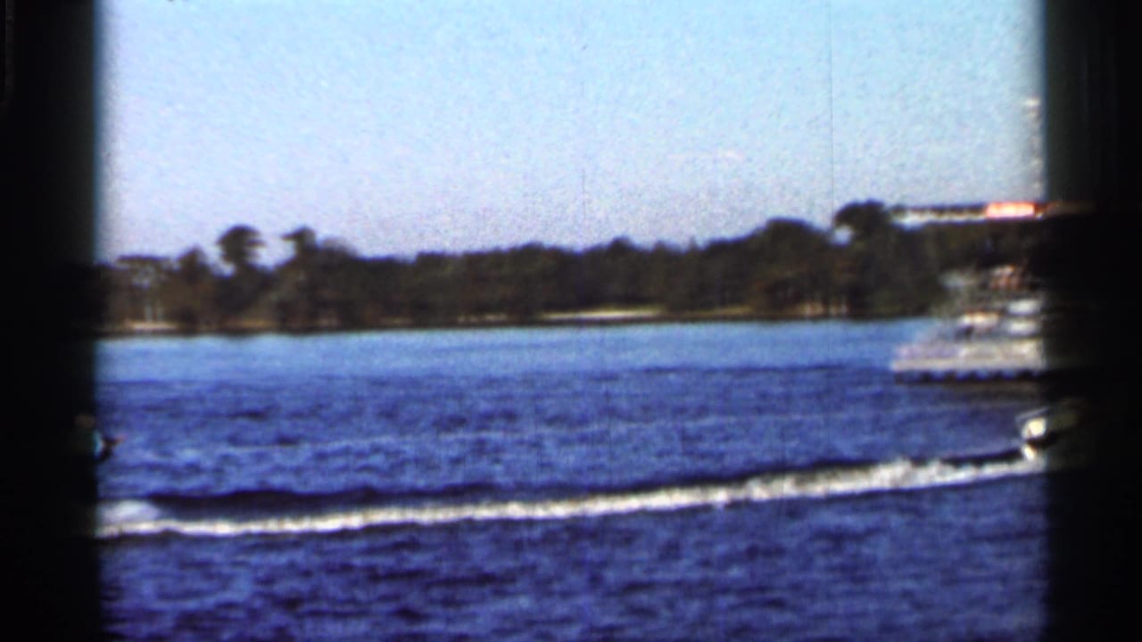 A speedboat moves across a Florida lake in 1966, leaving a long wake near a distant tree-lined shore.