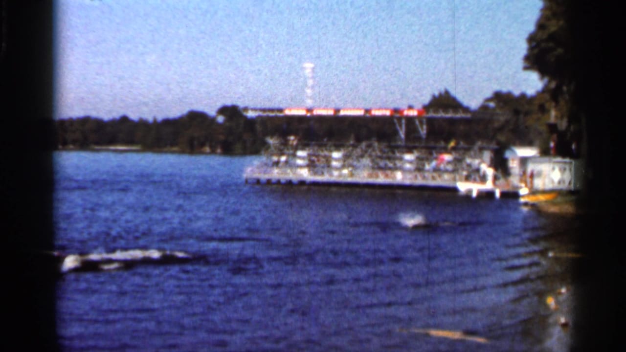 1966 Florida 8mm frame with the skier low on the lake surface while wake lines lead toward a docked platform.
