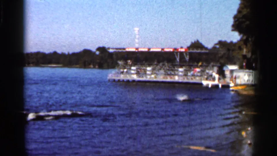 1966 Florida 8mm frame with the skier low on the lake surface while wake lines lead toward a docked platform.