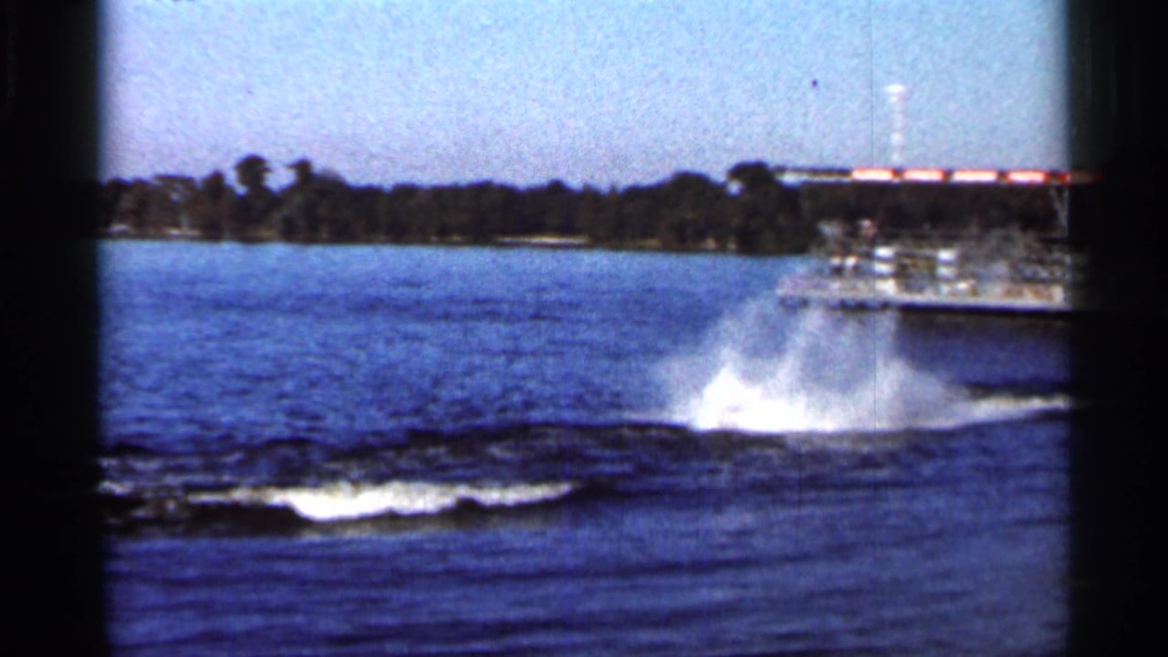 Motorboat and lake wake with a large splash near a tree-lined shore.