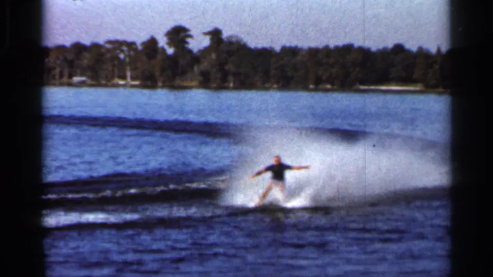 1966 Florida 8mm frame showing a man barefoot waterskiing across a lake, arms extended, with wake spray behind him.