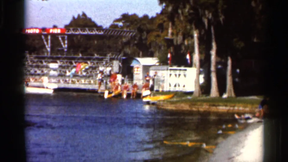 Boats and dock structures sit along the Florida Cypress Gardens waterfront, with palms and people visible near the shore.