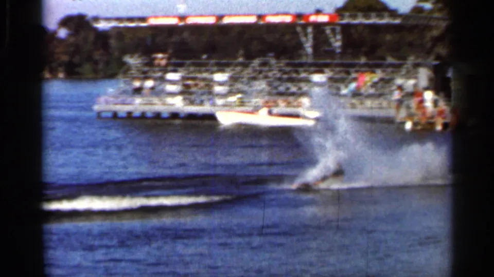 A water skier carves across the lake near docked boats and waterfront structures in 1966 Florida footage.
