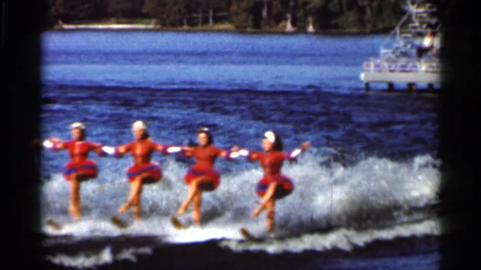 Four women in red-and-blue costumes continue a synchronized water-ski routine on a Florida lake in 1966 home-movie footage.